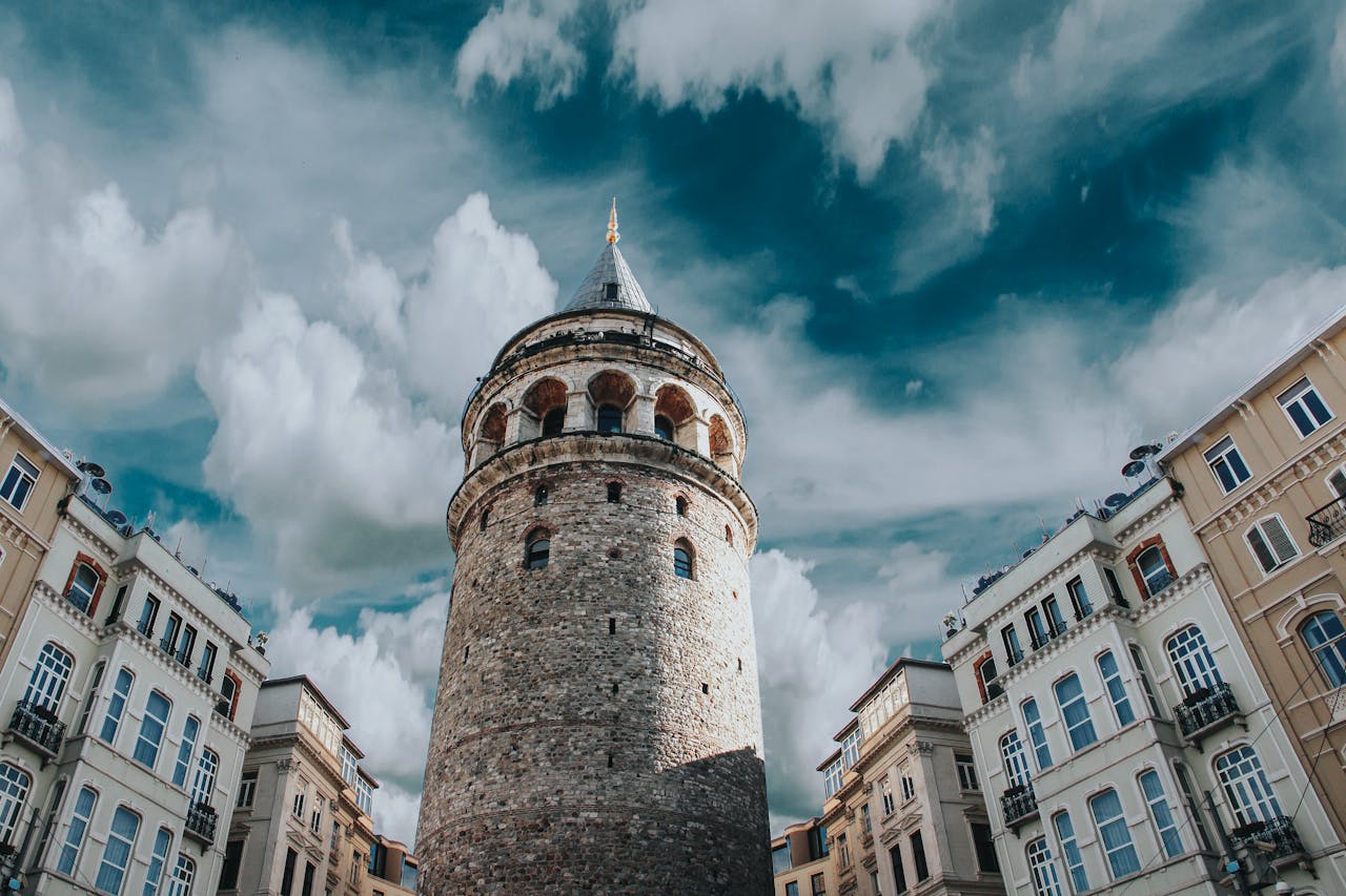 Home Captivating view of Galata Tower surrounded by historic architecture and dramatic clouds in Istanbul, Turkey.